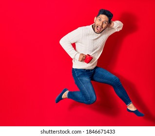 Young handsome latin man smiling happy drinking cup of coffee. Jumping with smile on face over isolated red background