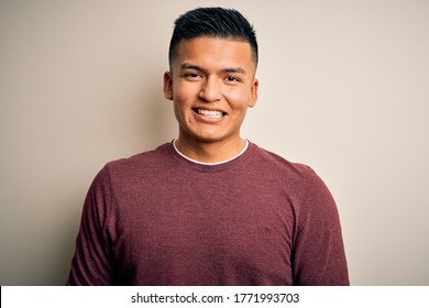 Junge, gut aussehende Latina-Mann, die einen ungezwungenen Pullover trägt, der auf isoliertem weißem Hintergrund steht und ein fröhliches und kühles Lächeln im Gesicht hat. Glücklicher Mensch.