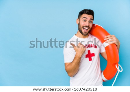 Young handsome lifeguard man isoalted points with thumb finger away, laughing and carefree.