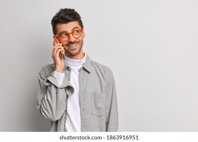 Young handsome male freelancer talks via mobile phone has cheerful expression enjoys mobile tariffs and connection wears spectacles shirt isolated on grey background with copy space for your text - Shutterstock ID 1863916951