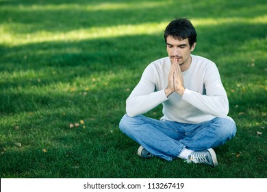 Young Handsome Male Sitting In The Lotus Pose Praying With Hands Pressed Toghether