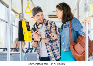 Young handsome male student helping attractive helpless female buying the ticket with ticket machine in modern tram during ride. Communication, acquaintance, friendship concept. - Shutterstock ID 1475465360
