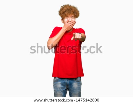 Young handsome man with afro hair wearing red t-shirt Laughing of you, pointing to the camera with finger hand over mouth, shame expression