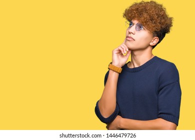 Young handsome man with afro wearing glasses with hand on chin thinking about question, pensive expression. Smiling with thoughtful face. Doubt concept.