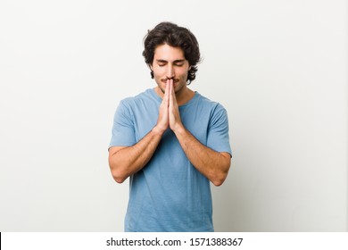 Young handsome man against a white background holding hands in pray near mouth, feels confident.
