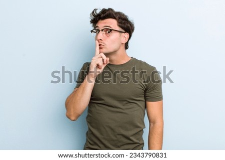 young handsome man asking for silence and quiet, gesturing with finger in front of mouth, saying shh or keeping a secret