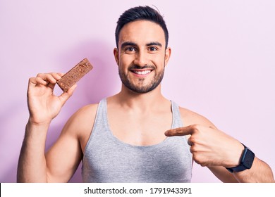 Young Handsome Man With Beard Eating Energy Protein Bar Over Isolated Pink Background Pointing Finger To One Self Smiling Happy And Proud