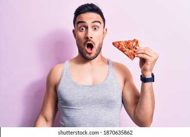 Young Handsome Man With Beard Eating Slice Of Italian Pizza Over Isolated Pink Background Scared And Amazed With Open Mouth For Surprise, Disbelief Face