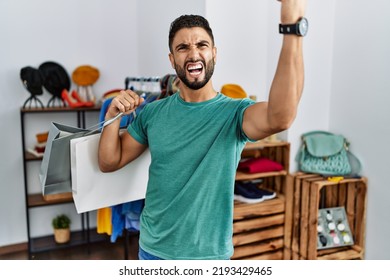 Young Handsome Man With Beard Holding Shopping Bags At Retail Shop Angry And Mad Raising Fist Frustrated And Furious While Shouting With Anger. Rage And Aggressive Concept. 