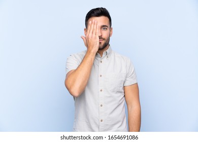 Young handsome man with beard over isolated blue background covering a eye by hand - Shutterstock ID 1654691086