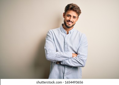 Young handsome man with beard wearing striped shirt standing over white background happy face smiling with crossed arms looking at the camera. Positive person. - Powered by Shutterstock