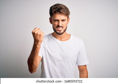 Young Handsome Man With Beard Wearing Casual T-shirt Standing Over White Background Angry And Mad Raising Fist Frustrated And Furious While Shouting With Anger. Rage And Aggressive Concept.