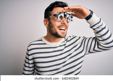 Young Handsome Man With Beard Wearing Optometry Glasses Over Isolated White Background Very Happy And Smiling Looking Far Away With Hand Over Head. Searching Concept.