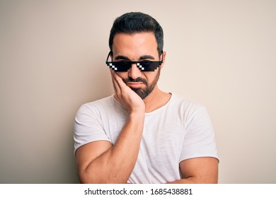 Young handsome man with beard wearing funny thug life sunglasses over white background thinking looking tired and bored with depression problems with crossed arms.