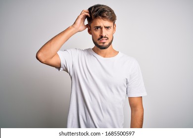 Young handsome man with beard wearing casual t-shirt standing over white background confuse and wonder about question. Uncertain with doubt, thinking with hand on head. Pensive concept. - Shutterstock ID 1685500597