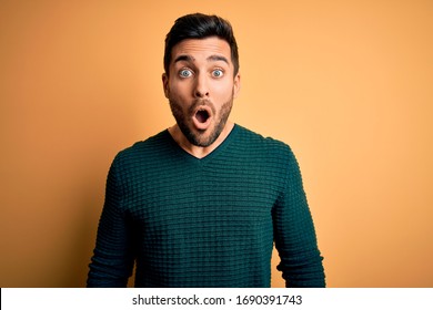 Young handsome man with beard wearing casual sweater standing over yellow background afraid and shocked with surprise expression, fear and excited face.