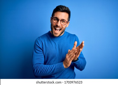 Young handsome man with beard wearing casual sweater and glasses over blue background clapping and applauding happy and joyful, smiling proud hands together - Shutterstock ID 1703976523