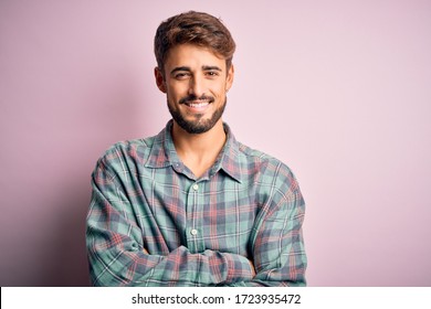 Young handsome man with beard wearing casual shirt standing over pink background happy face smiling with crossed arms looking at the camera. Positive person.