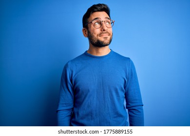 Young handsome man with beard wearing casual sweater and glasses over blue background smiling looking to the side and staring away thinking. - Shutterstock ID 1775889155