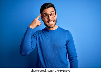 Young handsome man with beard wearing casual sweater and glasses over blue background Smiling pointing to head with one finger, great idea or thought, good memory - Shutterstock ID 1795915399