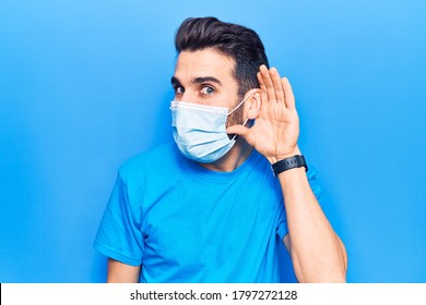 Young Handsome Man With Beard Wearing Medical Mask Smiling With Hand Over Ear Listening And Hearing To Rumor Or Gossip. Deafness Concept. 