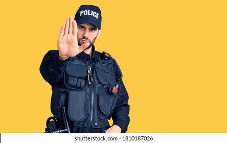 Young handsome man with beard wearing police uniform doing stop sing with palm of the hand. warning expression with negative and serious gesture on the face.  - Powered by Shutterstock