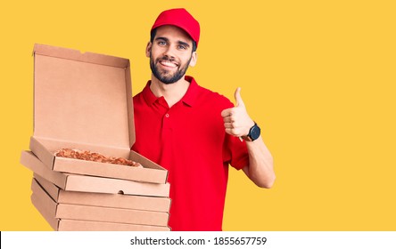 Young handsome man with beard wearing delivery uniform holding boxes with pizza smiling happy and positive, thumb up doing excellent and approval sign  - Shutterstock ID 1855657759