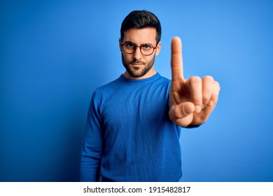Young handsome man with beard wearing casual sweater and glasses over blue background Pointing with finger up and angry expression, showing no gesture - Shutterstock ID 1915482817