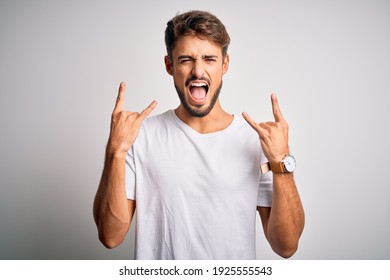 Young Handsome Man With Beard Wearing Casual T-shirt Standing Over White Background Shouting With Crazy Expression Doing Rock Symbol With Hands Up. Music Star. Heavy Concept.