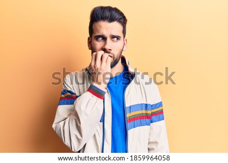 Young handsome man with beard wearing casual jacket looking stressed and nervous with hands on mouth biting nails. anxiety problem. 