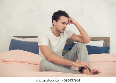 Young Handsome Man In Bedroom Sitting On Bed. Sad Man Thinking About Something. Nice Loft Interior