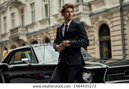 Young handsome man with black classic car wear black suit 