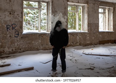 Young Handsome Man In Black Hoodie Smoking Vape White Smoke In Old Building At Winter With Snow On The Floor. Protest Man, Grunge And Unformal, No Face