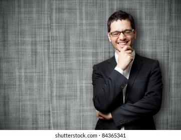 Young handsome man in black suit and glasses laughing against gray textured wall