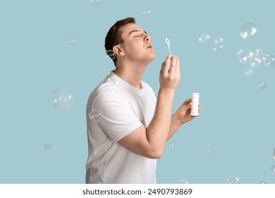 Young handsome man blowing soap bubbles on blue background - Powered by Shutterstock