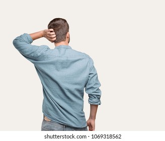 young handsome man, blue denim shirt, back pose and thinking or doubting . person isolated against monochrome background
