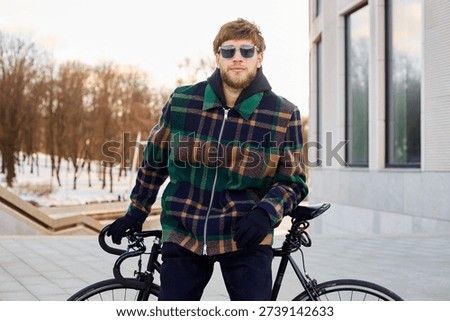 A young handsome man in a checkered jacket with sunglasses went for a bike ride.
