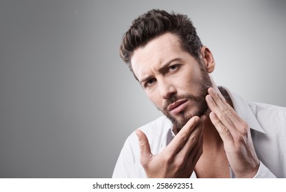 Young Handsome Man Checking His Face Skin And Touching His Beard