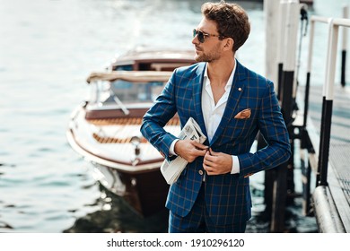 Young handsome man in classic suit over the blurred lake buttoning his jacket - Shutterstock ID 1910296120
