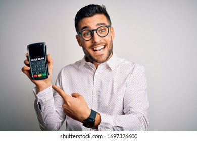 Young handsome man doing payment using dataphone over isolated white background very happy pointing with hand and finger