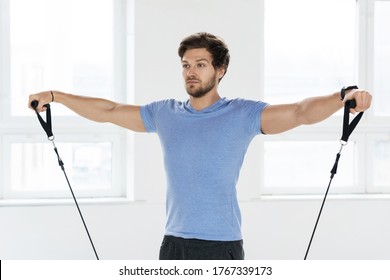 Young Handsome Man During Workout With A Resistance Rubber Bands In The Gym. Shoulder Lateral Raise Exercise.