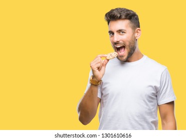 Young handsome man eating chocolate chips cookie over isolated background with a confident expression on smart face thinking serious