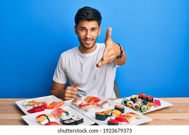 Young Handsome Man Eating Sushi Sitting On The Table Smiling Friendly Offering Handshake As Greeting And Welcoming. Successful Business. 