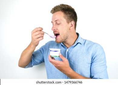 young handsome man eats yogurt holding spoon close to his mouth on isolated white background