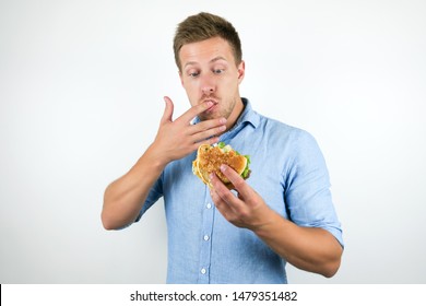 Young Handsome Man Enjoying Cheeseburger From Fast Food Restaurant Licking His Fingers While Eating On Isolated White Background