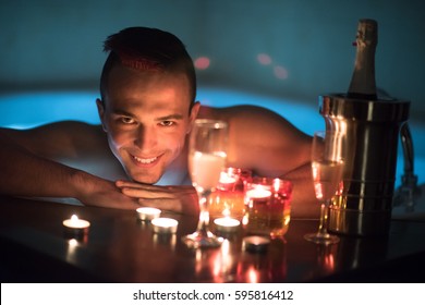 young handsome man enjoys relaxing in the jacuzzi with candles and champagne at luxury resort spa - Shutterstock ID 595816412