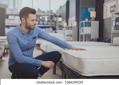 Young Handsome Man Examining Orthopedic Mattress On Sale At Furniture Store, Copy Space. Attractive Male Customer Buying New Bed At Homeware Supermarket. Consumerism, Home Concept