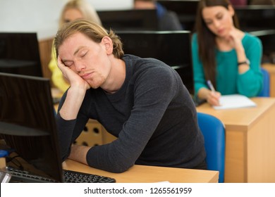 Young handsome man falling asleep during boring lecture at university. Cute male student sitting at table with personal computer, leaning head on hand and sleeping while other student writing. - Powered by Shutterstock