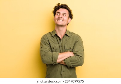 young handsome man feeling happy, proud and hopeful, wondering or thinking, looking up to copy space with crossed arms - Powered by Shutterstock