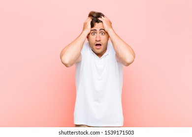 young handsome man feeling horrified and shocked, raising hands to head and panicking at a mistake against pink background - Shutterstock ID 1539171503